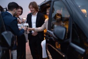 Group of business partners celebrating with alcohol near cars at night